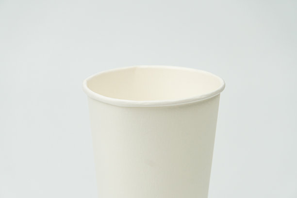 浅灰色的表面上放着一个白色的陶瓷或瓷杯，杯子边缘圆润。杯子略微倾斜，展示了其内侧的曲线。照片中没有其他物品可见，拍摄于室内。图片下载