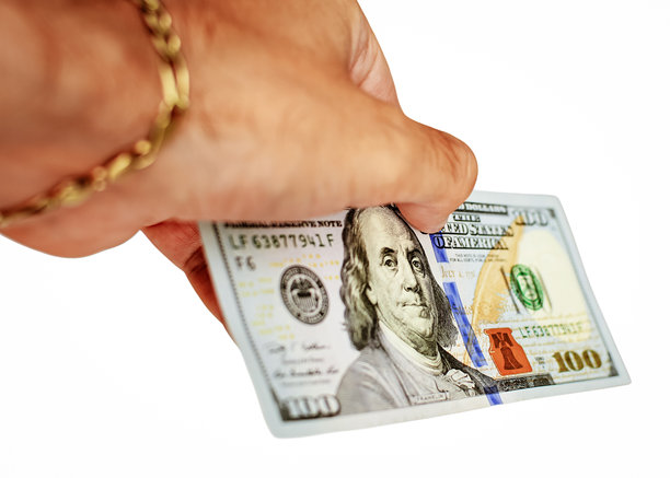 一只手握着一张崭新的100美元钞票的特写图像，代表着金融交易、经济交换以及现金在个人和商业财务中的力量。库存照片图片下载