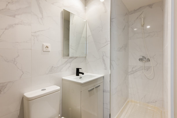 紧凑型浴室，配有大理石墙砖、白色洗手盆、黑色水龙头和带玻璃墙的淋浴间。图片下载