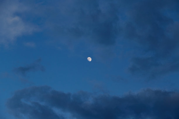 月光轻柔地照亮了深蓝色天空中云朵的边缘。这张照片传达了一种宁静、孤独和夜晚的魔力。图片下载