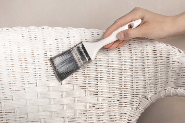 藤椅绘画。手握画笔，用白色油漆涂抹或给藤条上家具清漆。特写照片图片下载