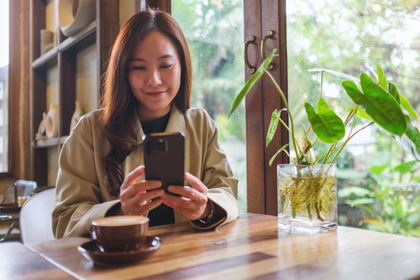 在咖啡馆里，一位女性手持手机并使用它的肖像照片图片下载