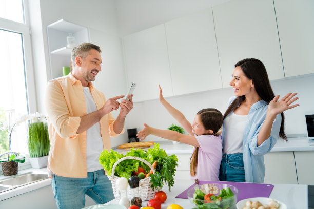 快乐的爸爸妈妈和小女儿在家厨房一起拍照做饭的照片图片下载