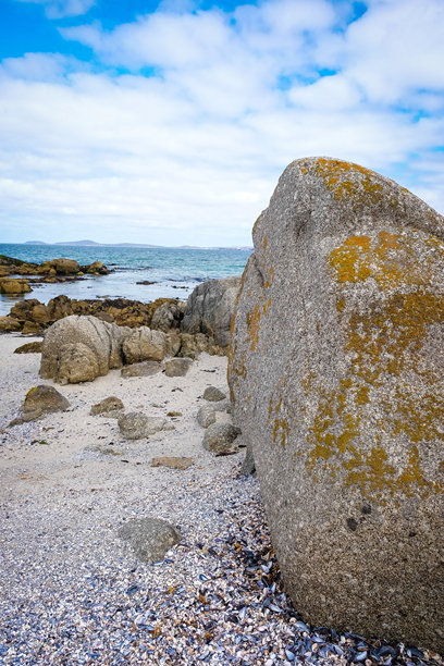 前景聚焦于大石头和沙子。低潮时的岩石海滩。自然照片，蓝天和白云映入眼帘。图片下载