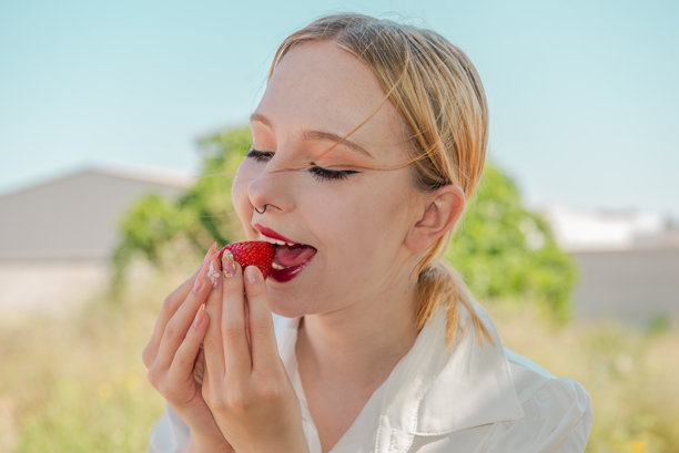 年轻女性青少年露出美丽的牙齿，咬着新鲜美味的草莓，特写，选择性对焦。适合社交网络的夏季照片。维生素健康小吃。图片下载