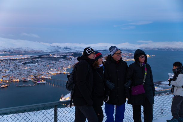 一群老年游客在乌尔斯基特点拍摄团体照片，背景是特罗姆瑟的夜景。图片下载