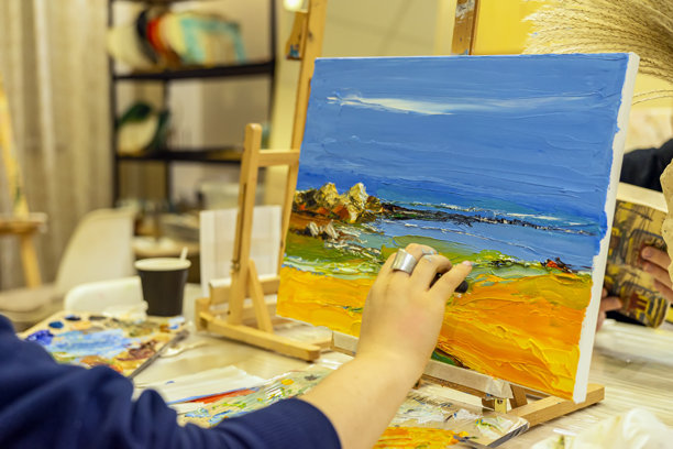 在舒适的艺术工作室环境中，使用调色刀手绘色彩斑斓的海景风景画。爱好、创造力、艺术表达和调色刀技巧的概念。图片下载