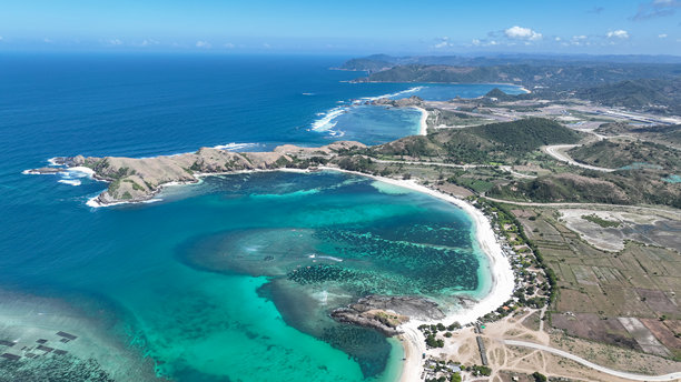令人惊叹的海岸线与郁郁葱葱的山丘和碧蓝的海洋在这张龙目岛的航拍照片中交汇。壮丽的景观邀请人们探索和享受宁静的时刻。图片下载