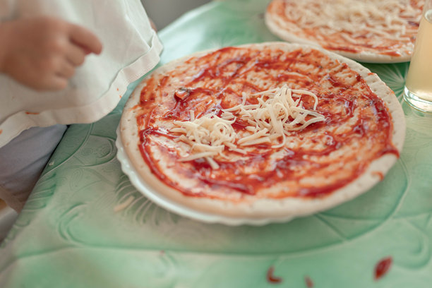 孩子在比萨饼面团上涂抹番茄酱和奶酪的特写照片图片下载