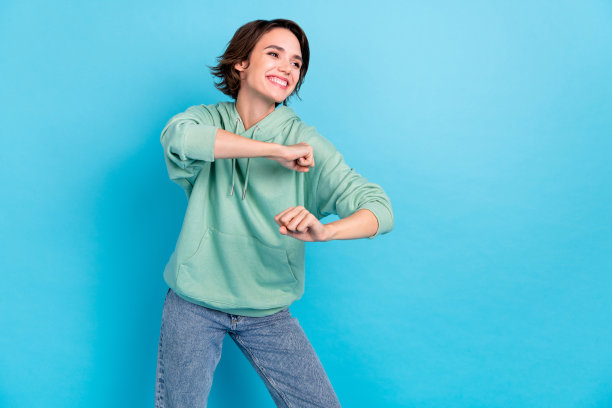 可爱的千禧年棕发女士穿着毛衣和牛仔裤在蓝色背景下跳舞的照片图片下载