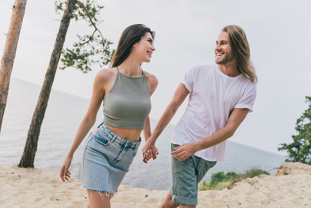 可爱的两个人在户外海水旁手挽手享受良好天气散步的照片图片下载