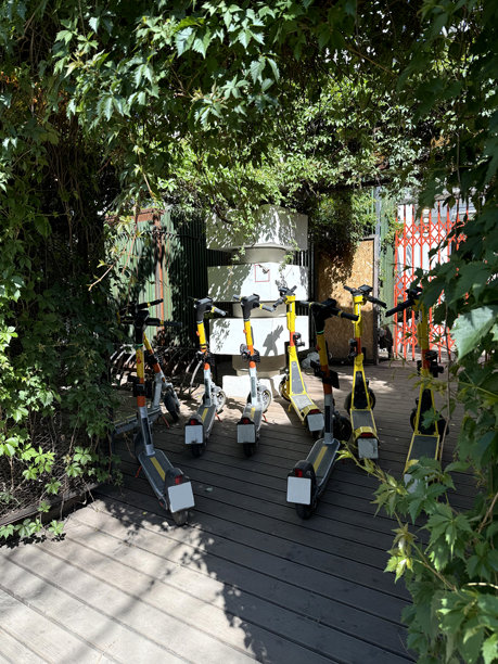 停放在树荫下的电动滑板车。现代城市交通概念。手工移动照片，选择性对焦，强烈阳光，非人工智能。图片下载