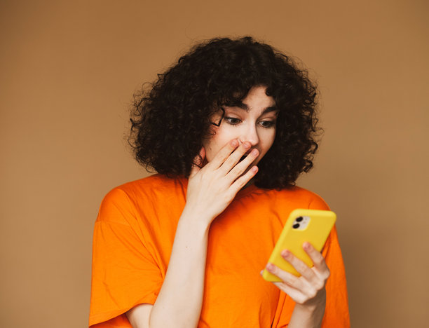 生活方式、科技与人：一位愉快的年轻卷发女性正在用手机聊天的照片。图片下载