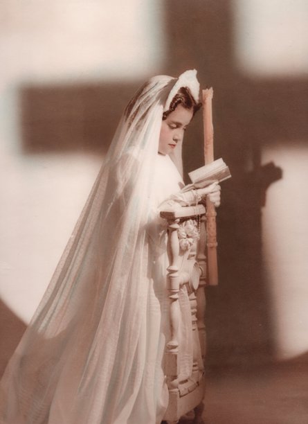 1940年代的复古照片，展示了一位跪着的小女孩，身穿第一次圣餐的服装，正在向上帝祈祷。图片下载