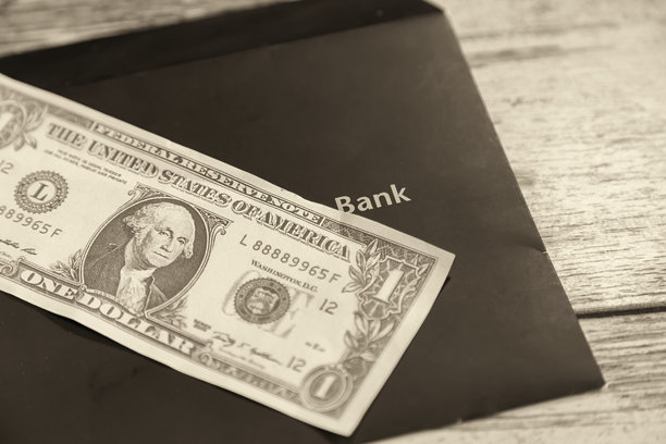 一美元在阳光下躺在一个黑色信封上，信封上写着“银行”，特写，黑白照片，银行贷款与支付，通货膨胀和存款。图片下载