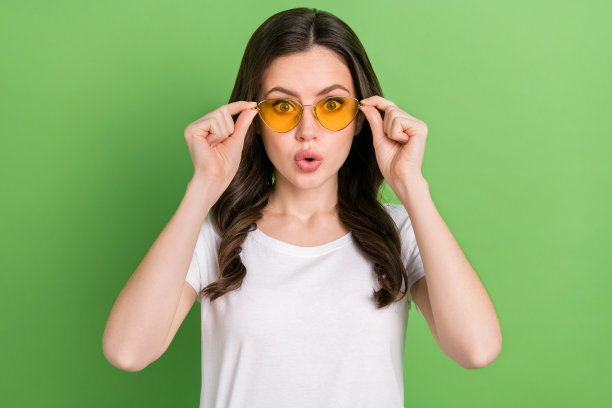 穿着白色T恤、戴着深色眼镜、眼睛大大的可爱惊讶女性的照片，背景为绿色。图片下载