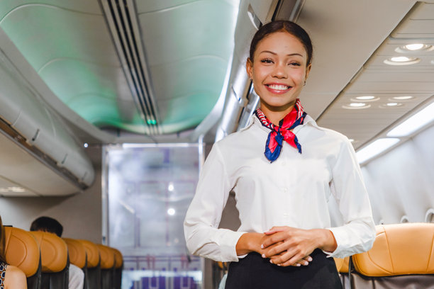 微笑的空乘人员站在飞机过道上，提供机上服务。代表了航空公司的热情好客、安全和对乘客的关怀。非常适合旅行行业的视觉素材。图片下载