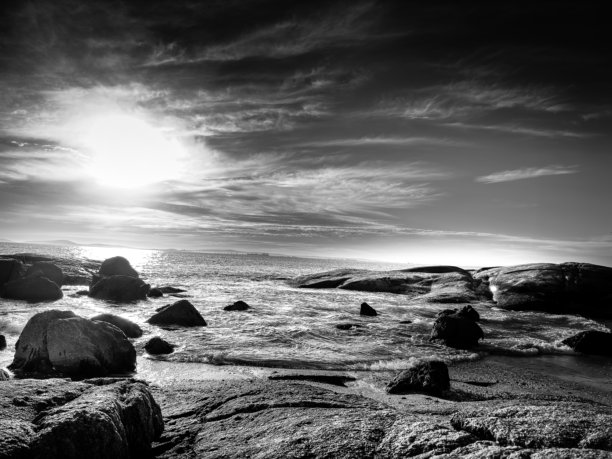 一张黑白照片展示了南非朗格班的海滩风景，夕阳的倒影映在水面上。风景壮观，背景照片展现了生活的平衡——阴郁的天空与自然之美。照片拍摄于2025年1月25日。图片下载