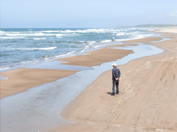 在五月的日本海，一个七十多岁的日本男子在微风拂面的春日里独自漫步在海滩，航拍照片展现了波浪和宁静的孤独。图片下载