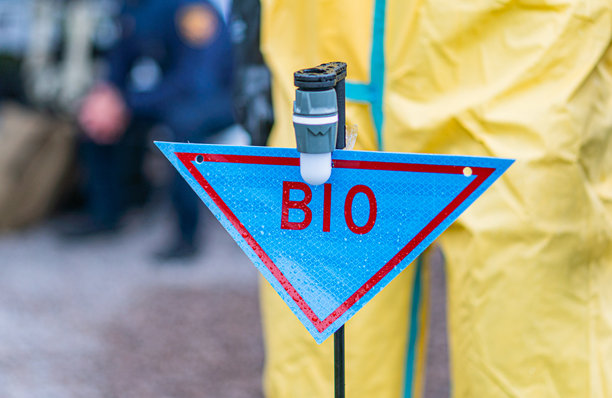 户外场景，部分遮挡的生物危害标志，穿着白色全身防护服的人，砾石地面，真实照片图片下载