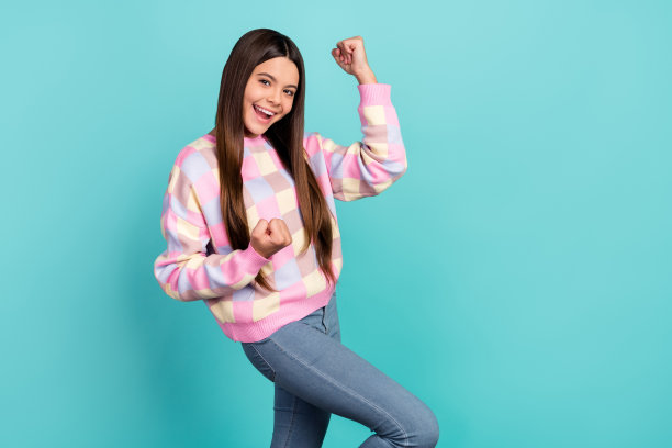 年轻女孩侧面照片，庆祝胜利，双拳紧握，背景为青绿色。图片下载