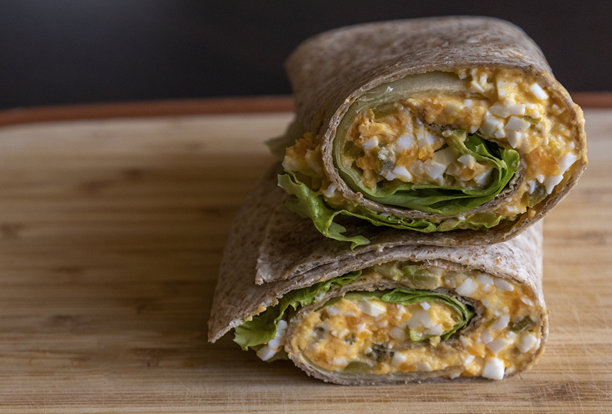 健康早餐的魔鬼蛋卷放在木砧板上。特写照片展示了一道新鲜、清淡的餐点，奶油魔鬼蛋整齐地包裹着。非常适合一天的健康开始。图片下载