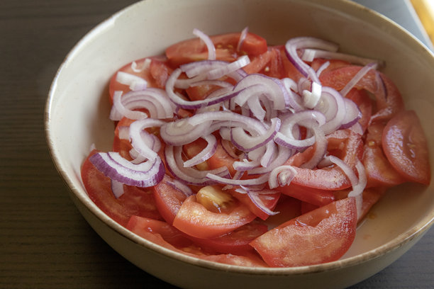 新鲜切片的番茄和红洋葱特写照片，盛在碗中。鲜红的番茄和紫色的洋葱圈。图片下载