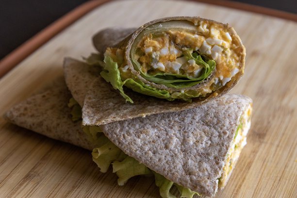 健康早餐的魔鬼蛋卷放在木砧板上。特写照片展示了一道新鲜、清淡的餐点，奶油魔鬼蛋整齐地包裹着。非常适合一天的健康开始。图片下载