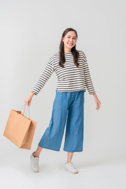 一位穿着条纹衬衫的年轻女性面带灿烂的笑容，手里提着购物袋，洋溢着快乐和兴奋。她愉悦的表情和休闲的风格使这张图片非常适合零售和时尚。图片下载
