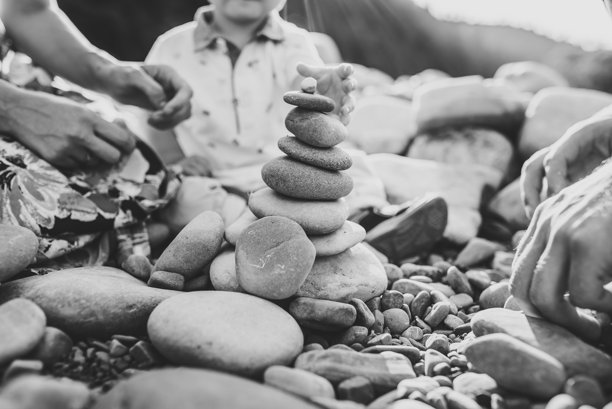 母亲、父亲和婴儿儿子坐在湖边的石头上玩耍。孩子与父母亲密互动。快乐的家庭假期，夏日黄昏时分。一起度过美好时光。黑白照片。图片下载