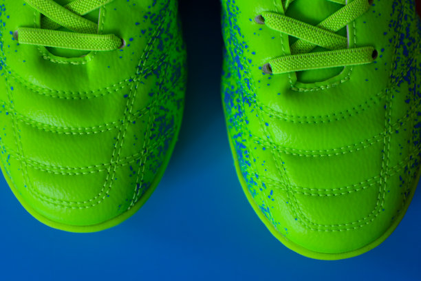 鲜艳的绿色足球鞋上点缀着蓝色斑点，静置在蓝色背景上，展示出清晰的缝线和材质纹理。这张照片非常适合展示运动鞋、足球装备或积极的生活方式。图片下载