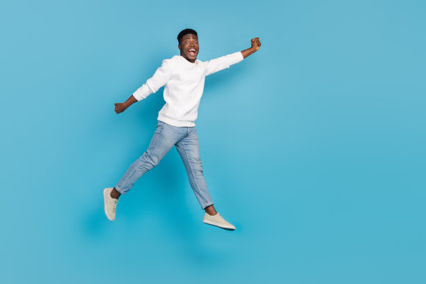 惊讶且满意的人在蓝色背景上跳起飞来，双手举起的全身照片图片下载