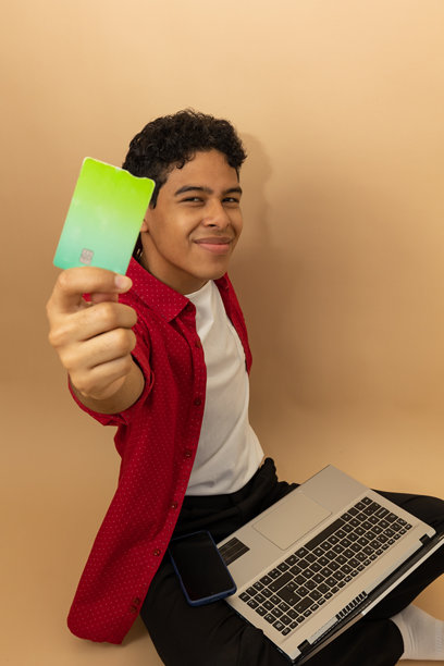 一位快乐的年轻拉丁裔男子在浅棕色背景前展示他的购物卡的竖版图片图片下载