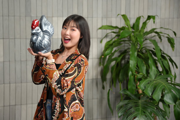 一位穿着巴蒂克的印尼亚洲女性，手持一只鸡形储蓄罐。照片的概念是将钱存入储蓄罐。图片下载