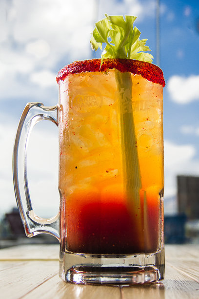 一杯色彩鲜艳的米切拉达鸡尾酒，具有引人注目的分层效果，配有芹菜装饰。这张图片捕捉了夏日清爽和庆祝聚会的精髓。图片下载