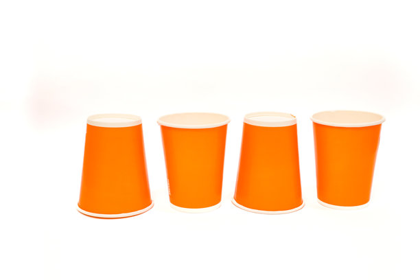 一张极简风格的库存照片，展示了四个鲜艳的橙色纸杯整齐排列在干净的白色背景上，适用于多种用途。图片下载