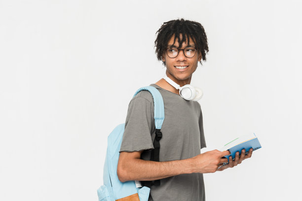 微笑的男孩，高中男学生，背着书包，手里拿着打开的书和笔记本，孤立在白色背景上，目光空洞，留出广告的空白空间。教育回归校园的概念。图片下载
