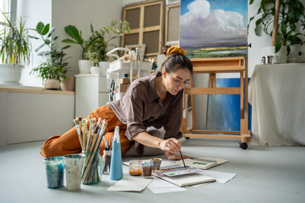 灵感满满的创意女孩插画师在艺术工作室的地板上用水彩在素描本上作画。图片下载