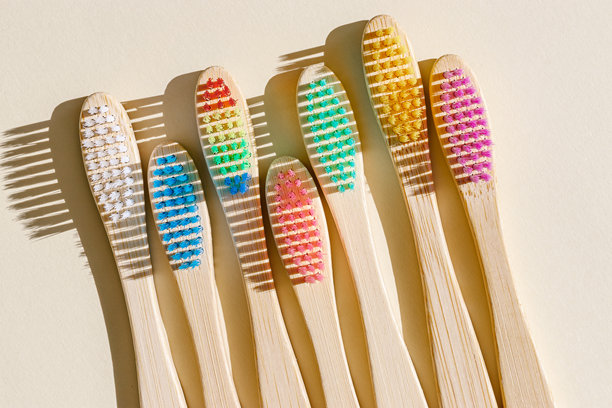 阳光下的米色背景上，特写的米色竹牙刷，刷毛呈现多种颜色。简约、卫生和环保的替代品，俯视照片，极简风格平铺。图片下载