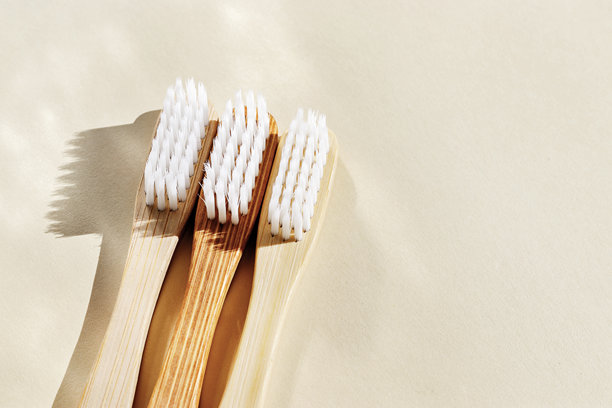 美观的米色竹牙刷，白色刷毛在米色背景下的阳光照射下。简约、卫生和环保的替代品，俯视照片，极简风格的中性色调平铺。图片下载