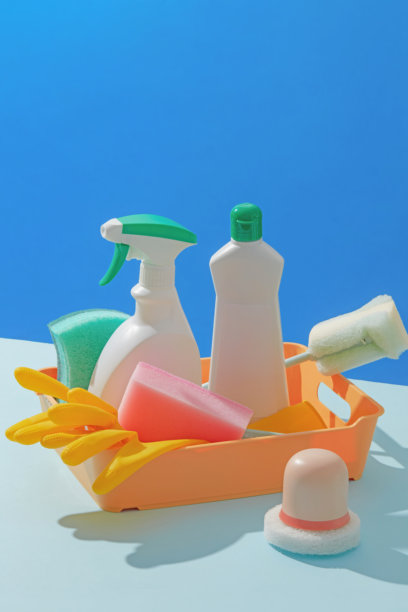 明亮而活泼的照片，展示了黄色篮子里装着塑料清洁瓶和工具，背景为蓝色，非常适合用于清洁产品的广告。产品瓶未贴标签，留有空白空间供设计使用。图片下载