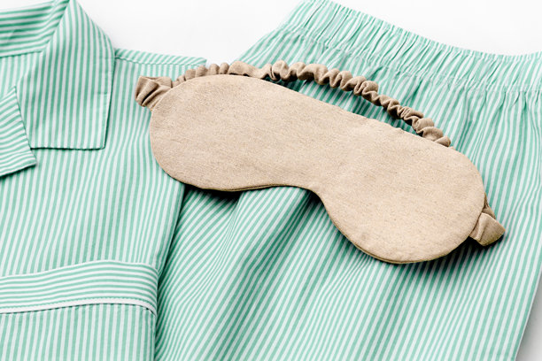 从上方拍摄的米色睡眠眼罩放在折叠的绿色条纹睡衣上，特写纹理照片。极简风格，舒适与安逸的时尚睡衣。自我护理，健康，宁静的生活方式，家居美学。图片下载