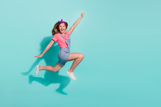 穿着条纹T恤和短裤的疯狂青少年孩子在青色背景上跳跃并举起手飞翔的全身照片图片下载