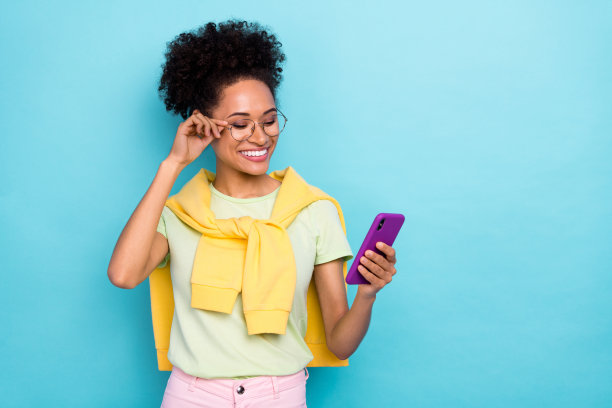 年轻快乐的非洲女孩侧面照片，使用智能手机发送短信评论，背景为蓝色。图片下载