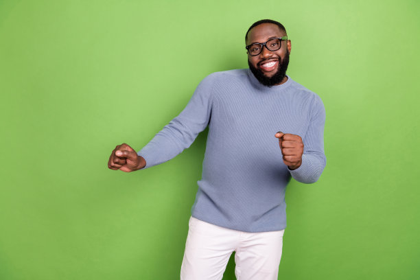 穿着灰色毛衣、戴着眼镜的迷人非洲男士在绿色背景下跳舞的照片图片下载