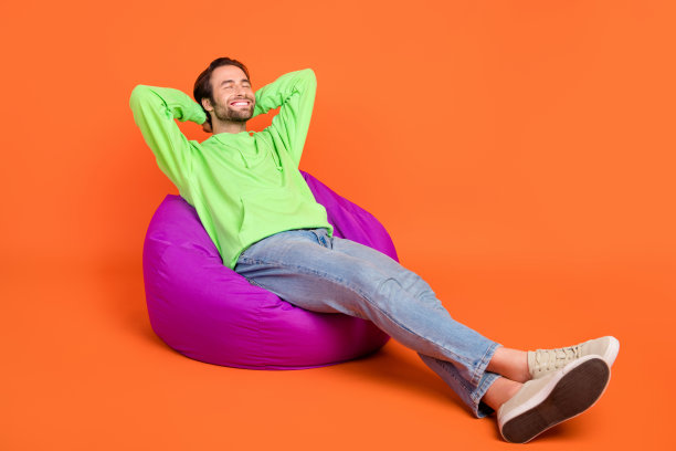 全身照片，棕发千禧一代男孩穿着绿色运动服、牛仔裤和鞋子，躺着睡觉，背景为橙色。图片下载