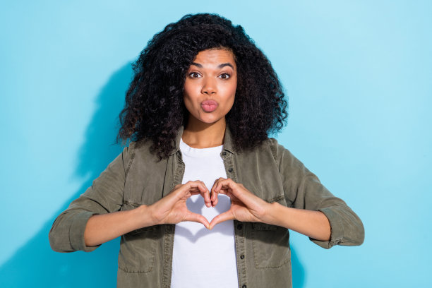 年轻非洲女士的照片，丰满的嘴唇送出空气之吻，浪漫约会，心形图案，背景为蓝色。图片下载