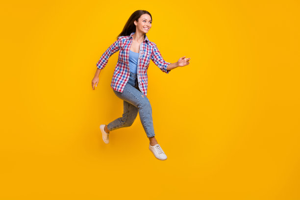 充满活力的可爱女士穿着格子衬衫在黄色背景下跳跃奔跑的全身侧面照片图片下载