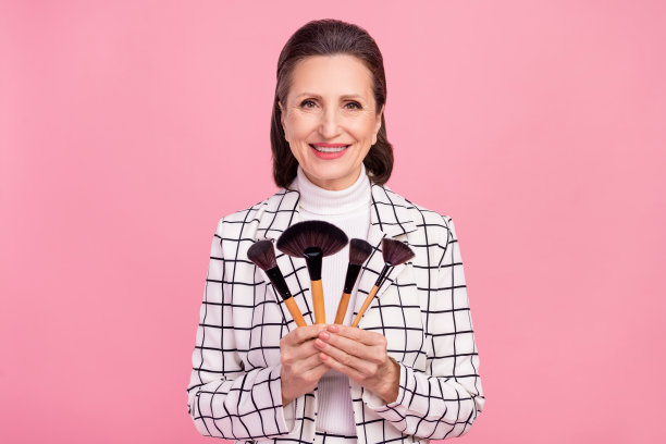 微笑的迷人女性在粉色背景上推荐化妆刷的照片图片下载