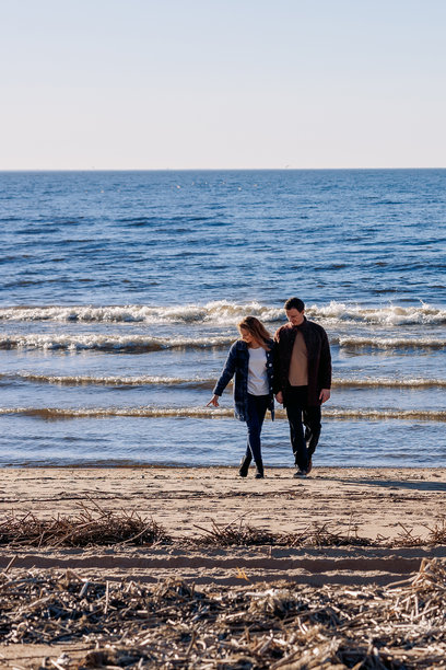 恩爱情侣在阳光明媚的秋日海滩上漫步。周末和生活方式的概念。竖版照片图片下载